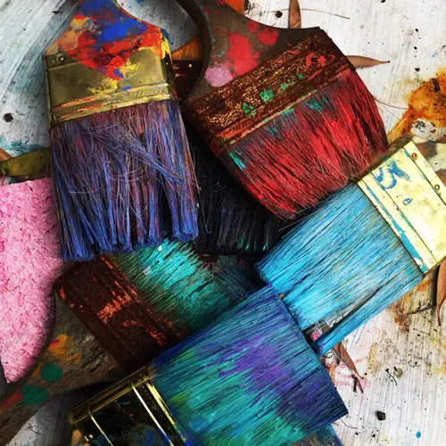 Various paint brushes and colorful paint splatters displayed on a wooden table.